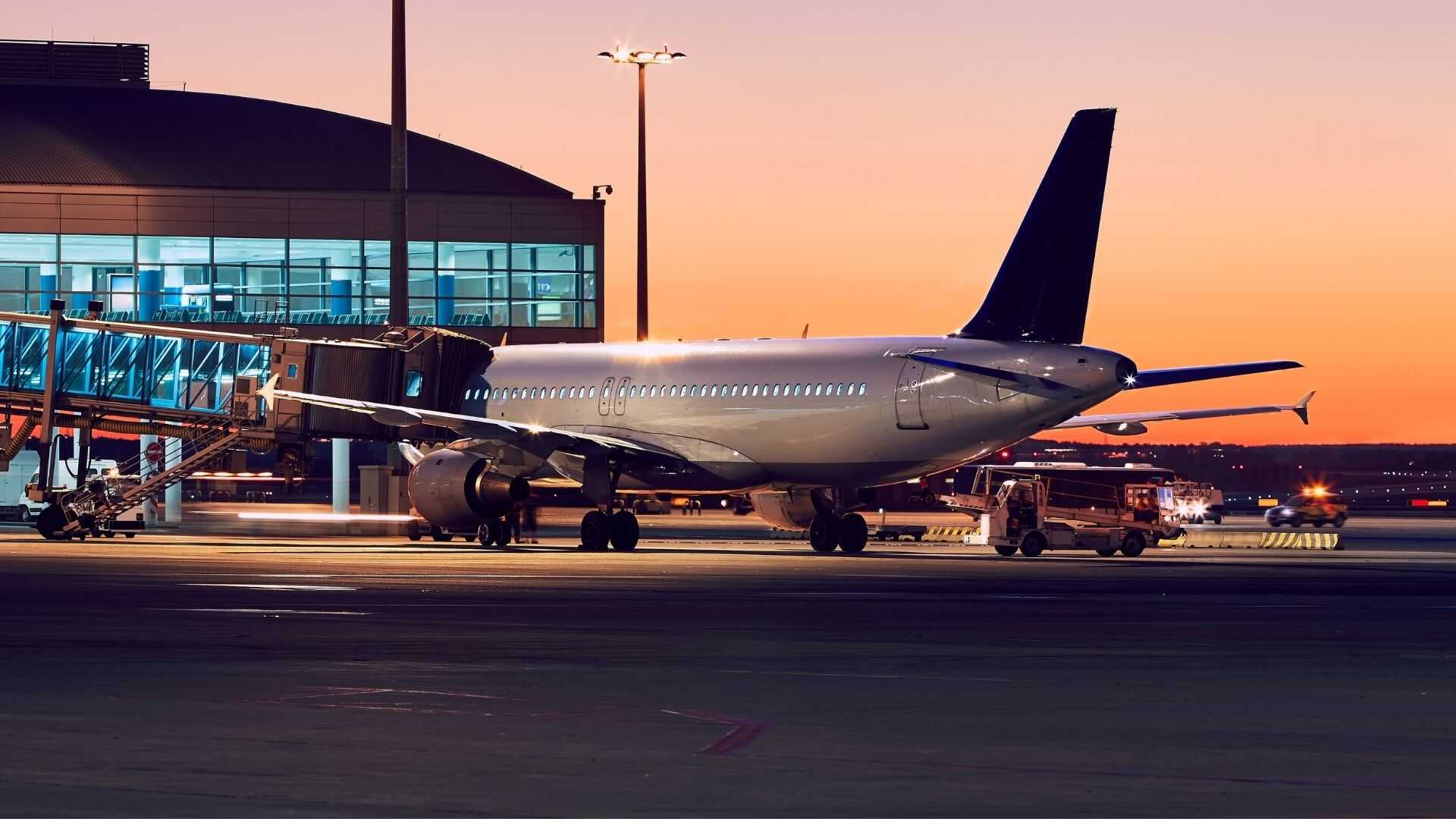 Commercial airliner connected to an airport VIP terminal bridge at sunset after a group charter flight arrival.